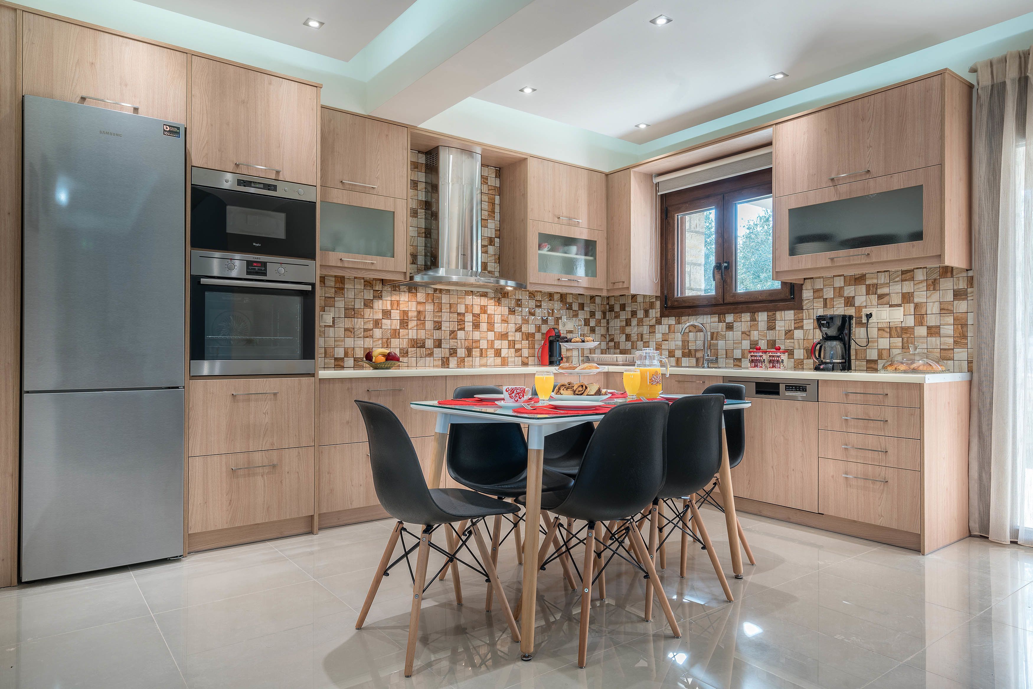 A modern kitchen with wooden cabinets, stainless steel appliances, and a dining area with black chairs.