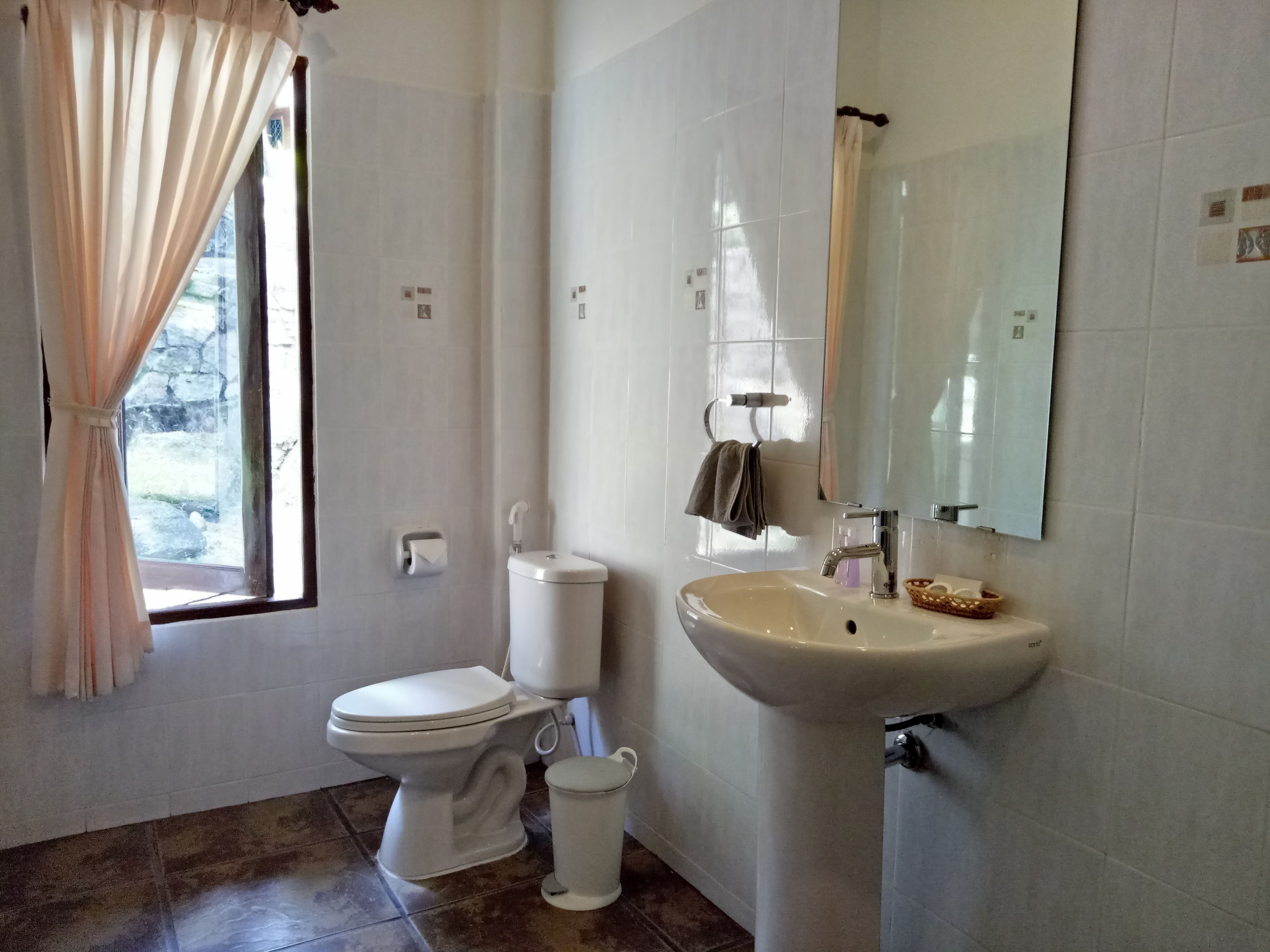 Une salle de bain avec des toilettes, un lavabo et une fenêtre avec des rideaux.