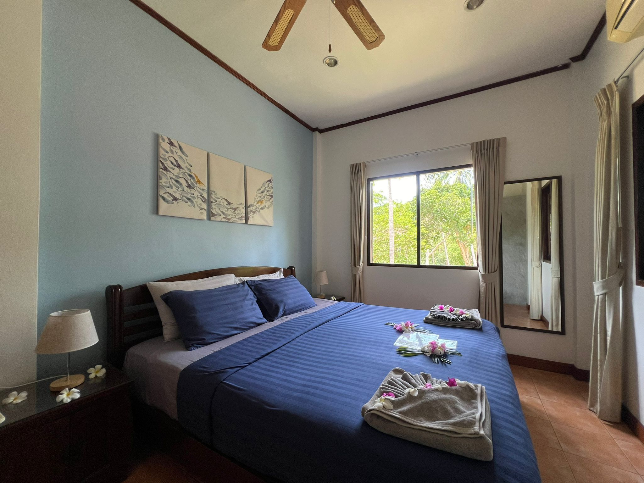 Habitación de hotel con una cama grande, una mesita de noche con lámpara, una ventana con cortinas y una obra de arte en la pared.