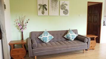 A living room with a grey sofa, two patterned cushions, a vase with dried flowers, and three wall art pieces depicting leaves.
