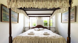 A four-poster canopy bed with floral bedding, a wooden headboard, and two bedside lamps.