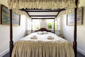 A four-poster canopy bed with floral bedding, a wooden headboard, and two bedside lamps. - Lehnsgaard Ranch (Gudhjem)