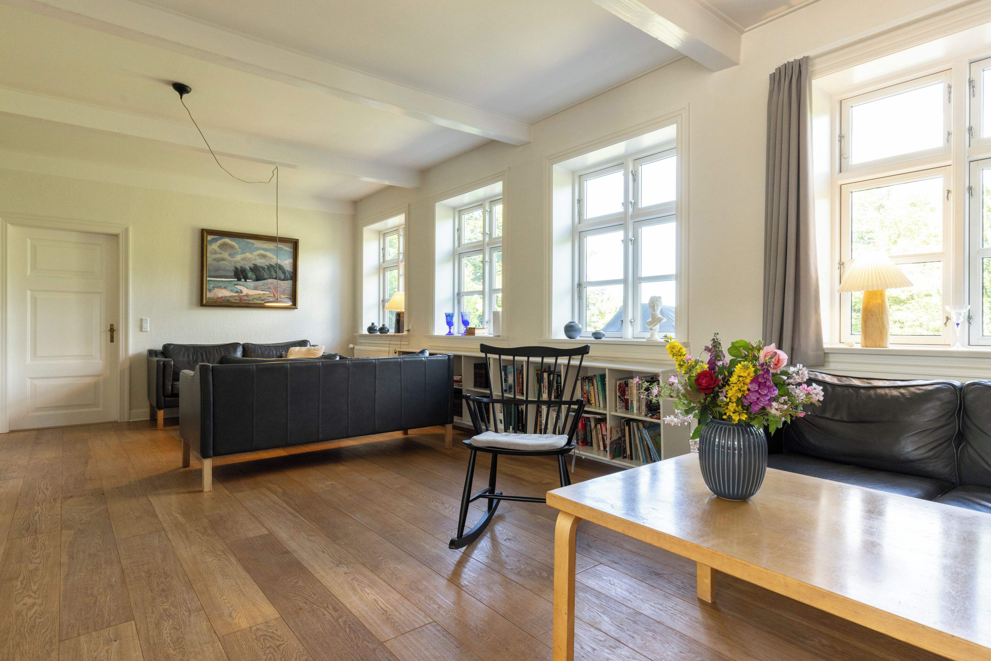 A spacious living room with a black leather sofa, a wooden coffee table, and a bookshelf filled with books.