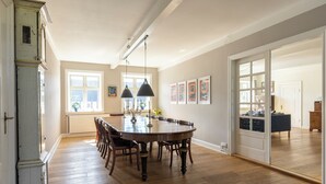 A spacious dining area with a large wooden table and chairs, a chandelier, and artwork on the walls.
