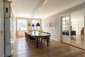 A spacious dining area with a large wooden table and chairs, a chandelier, and artwork on the walls. - Lehnsgaard Ranch (Gudhjem)