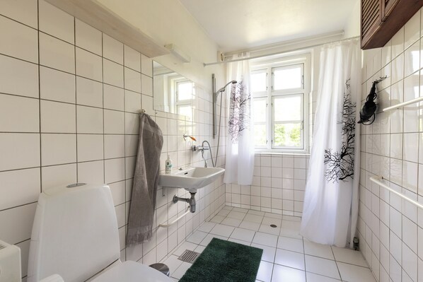 Un baño con lavamanos blanco, inodoro, ducha y ventana con cortinas.