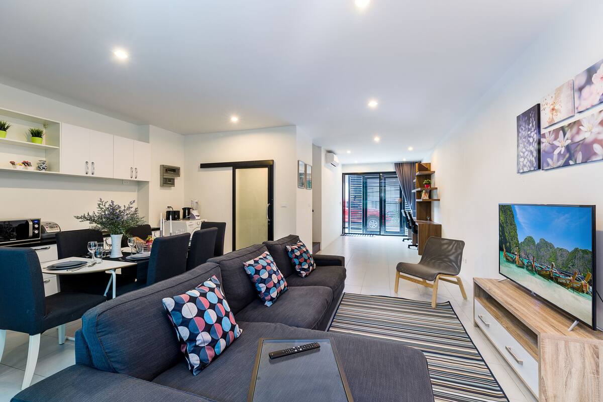 A modern living room with a grey sofa, a TV, and a dining area with a table and chairs.