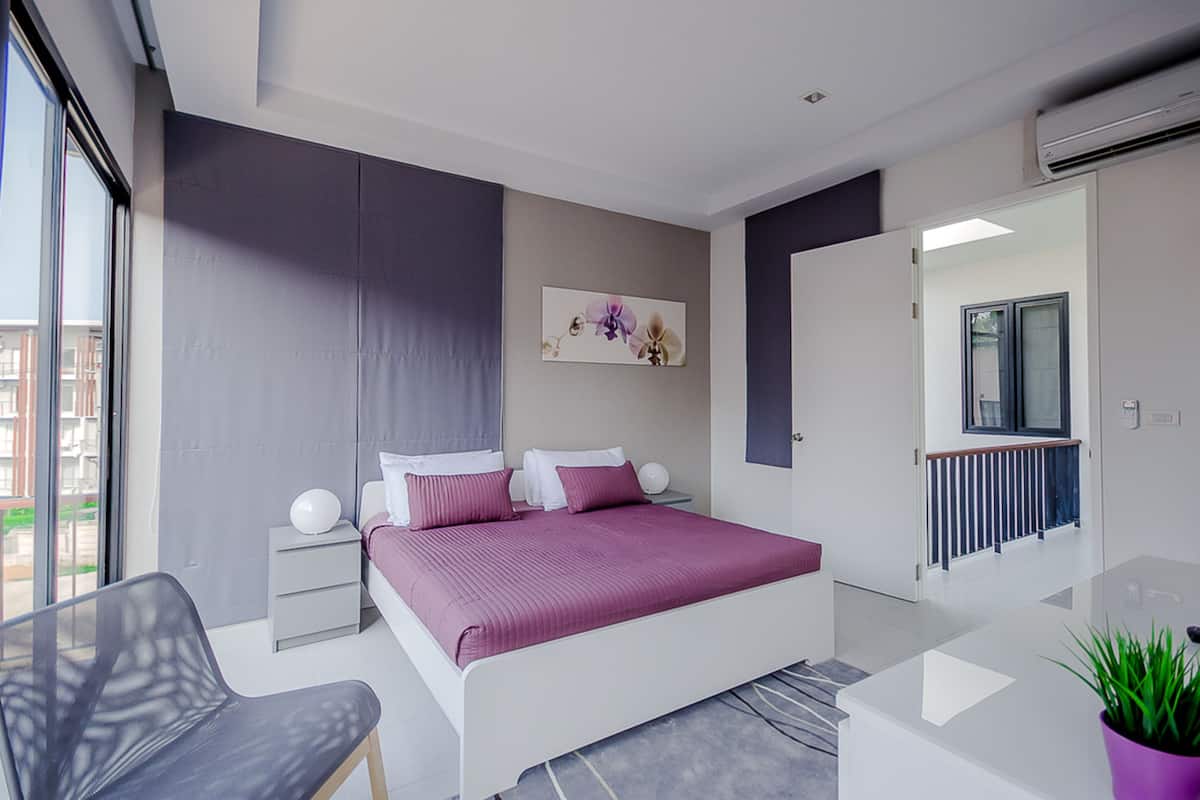 A modern bedroom with a bed, bedside tables, a chair, a potted plant, and a view of the outside.