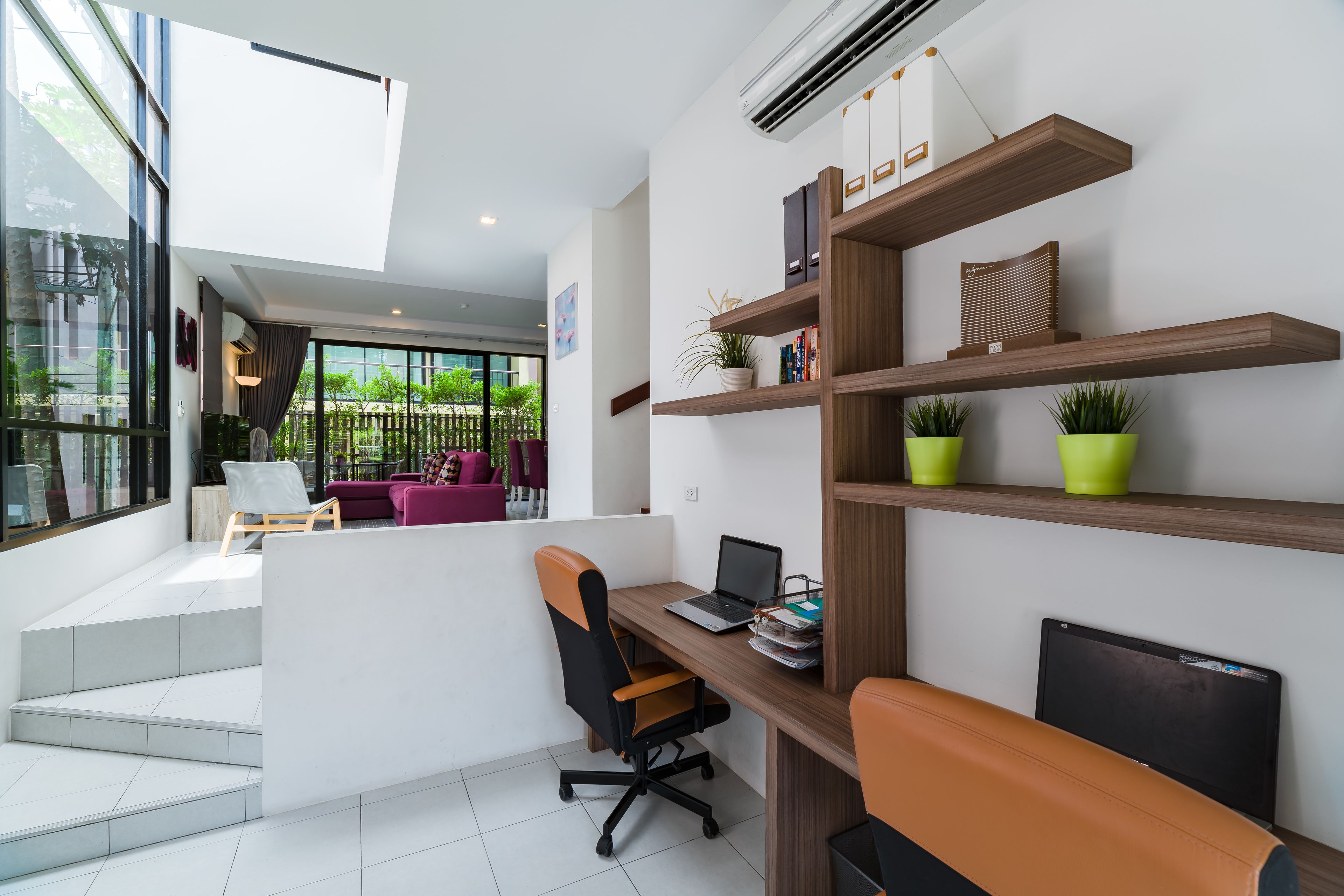 A modern office space with a desk, chair, and shelves with books and plants.
