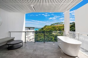 Ein modernes Badezimmer mit einer freistehenden Badewanne, einem runden schwarzen Tisch und einem Glastrennfeld mit Blick auf eine reizvolle Landschaft.