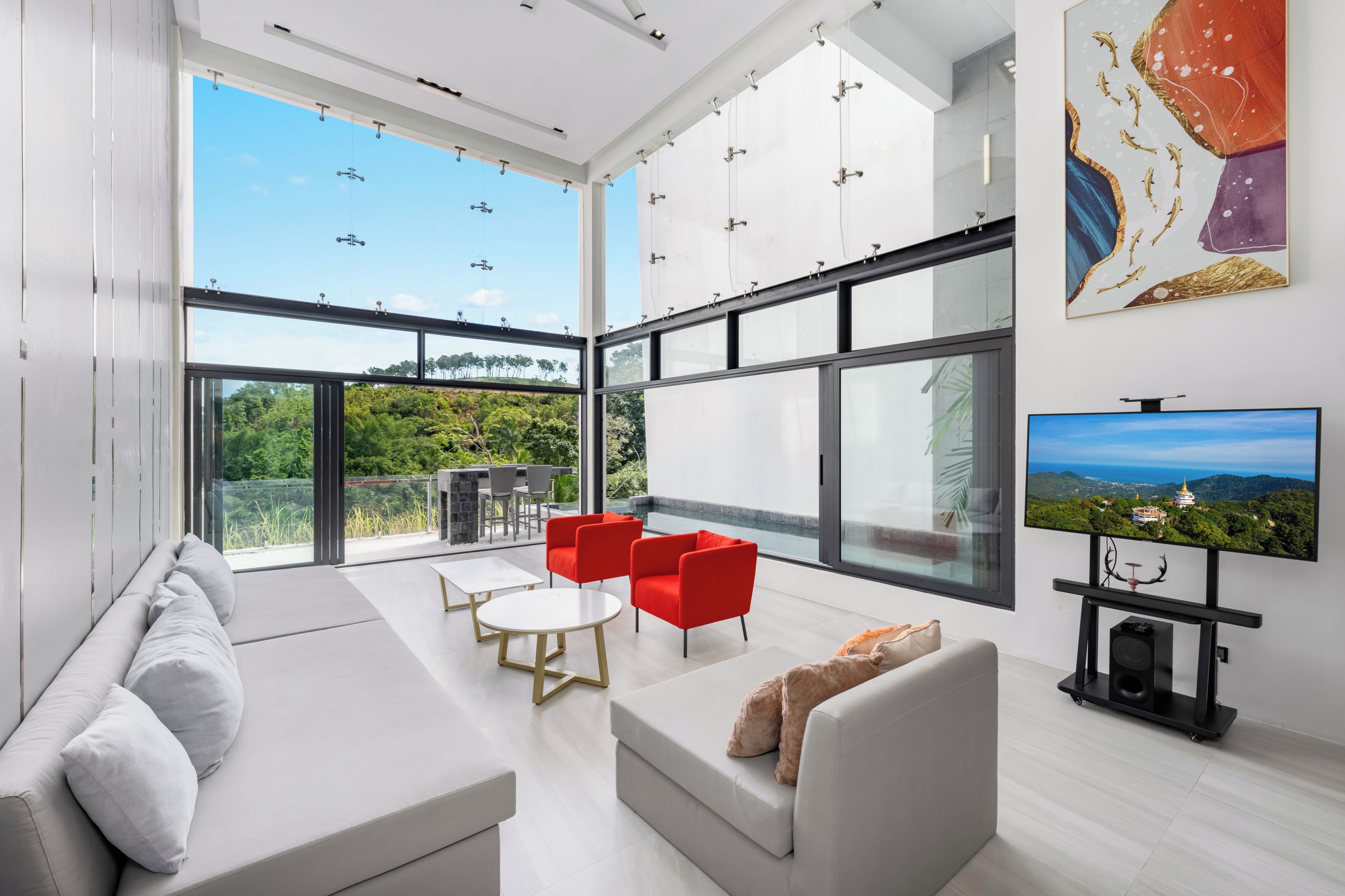 A modern living room with a large TV, seating area, and a view of greenery.