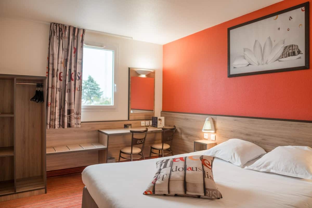 Une chambre d’hôtel comprenant un lit, un bureau, une chaise, une armoire, un miroir et une fenêtre.