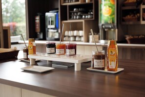 Un comptoir avec des pots de miel et de confiture, une bouteille de miel et, au fond, une machine à café.
