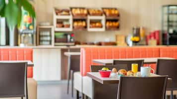 Ein Restaurant mit orangefarbenen Sitzbänken, einer Theke mit Speisenpräsentationen und Frühstücksangeboten auf einem Tisch.
