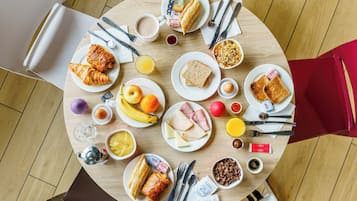 Una mesa redonda para comer con diversos alimentos de desayuno, como cruasanes, tostadas, huevos y frutas.