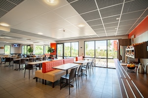 Una amplia cafetería con mesas altas, asientos acolchados rojos y grandes ventanales con vistas al exterior.