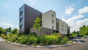 A modern hotel with a flat roof, a parking lot, and a landscaped garden area.