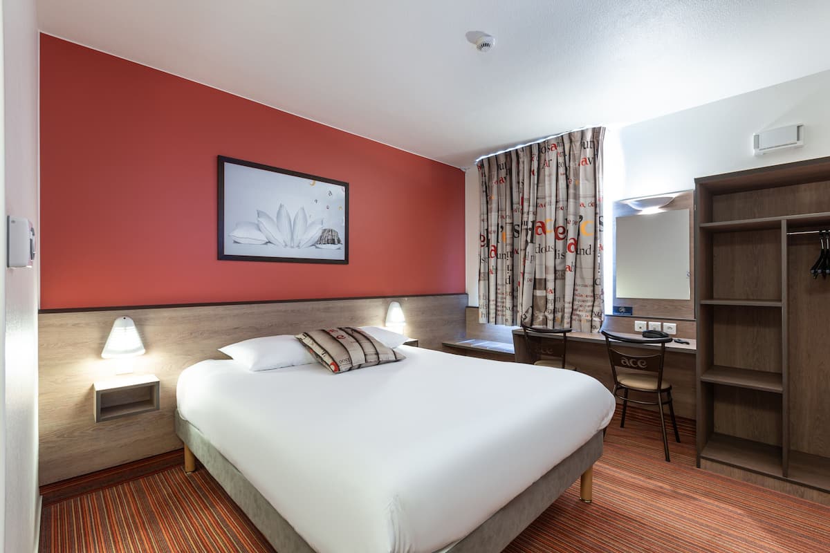 Une chambre d’hôtel comprenant un lit, un bureau, une chaise, une armoire et un tableau encadré au mur.