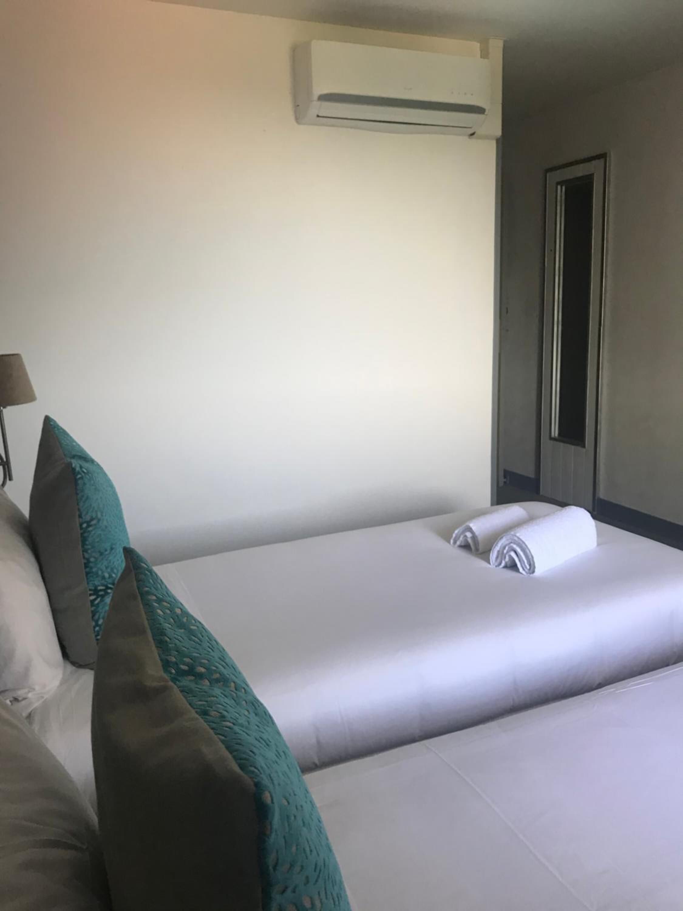 A hotel room with two beds, a wall-mounted air conditioner, a door, and a lamp.