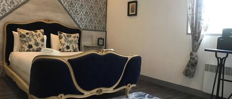 A bedroom with a large bed, a nightstand, a desk, and a patterned wall.