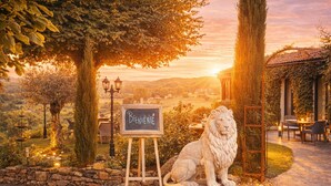 A stone pathway leading to a rustic outdoor seating area with a lion statue and a welcome sign. - Hôtel Bien-Etre Aux Cyprès de Marquay (Marquay)