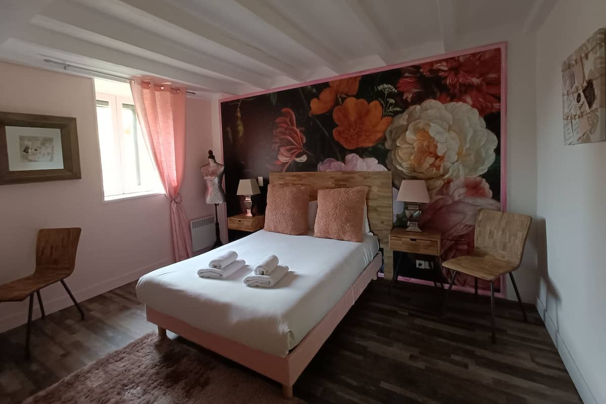Une chambre à coucher comprenant un lit, une chaise, une table de chevet, une lampe et une grande fresque murale à motifs floraux.