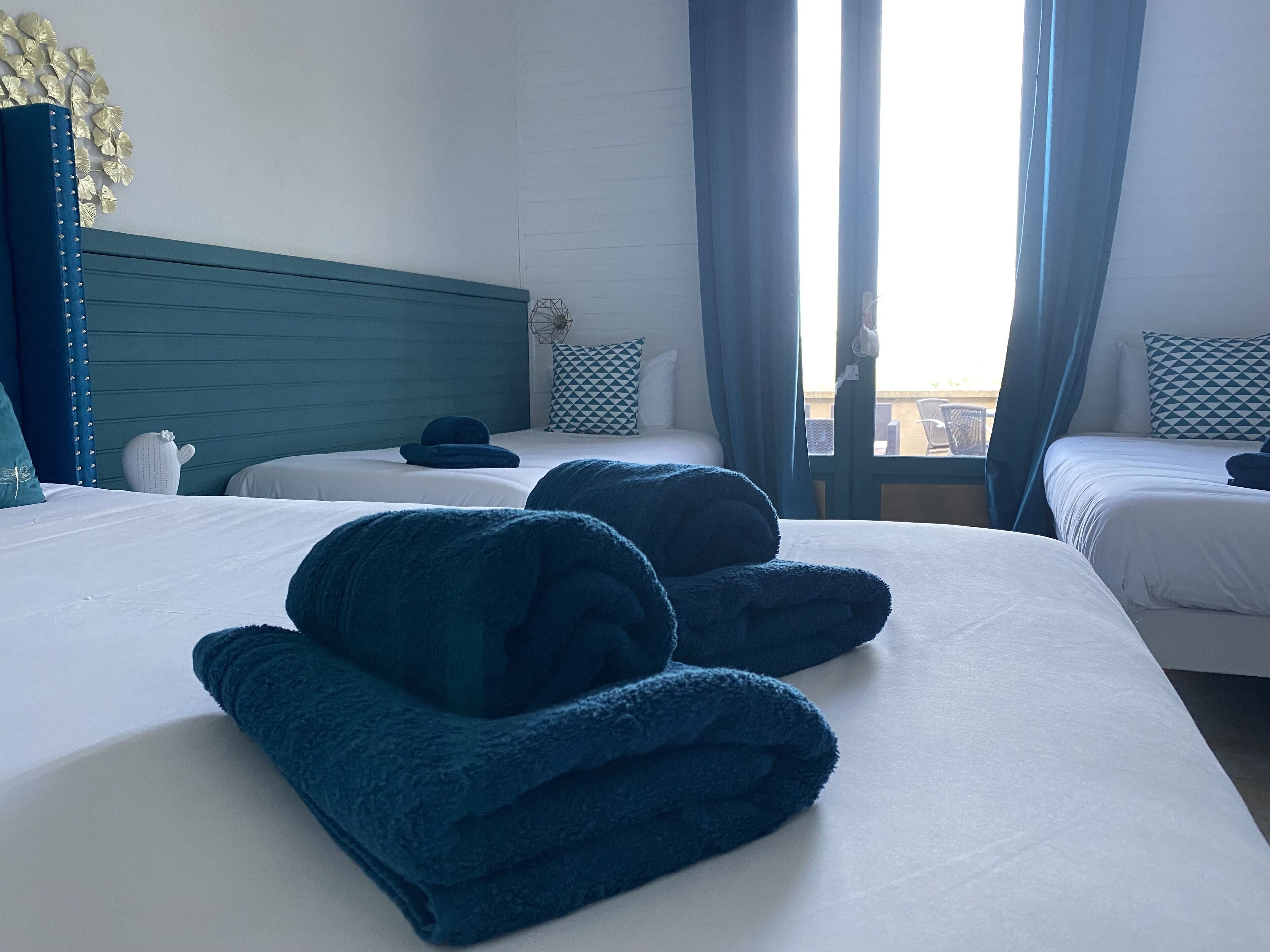 Habitación de hotel con dos camas, vista al exterior y un cabecero azul.