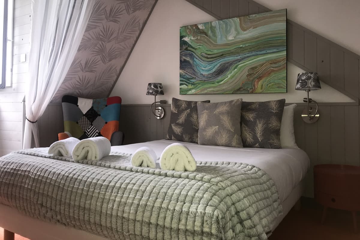 Une chambre à coucher moderne avec un grand lit, un tableau abstrait aux couleurs vives et une vue sur l’extérieur.