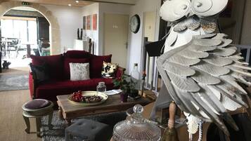 Un salon avec un canapé rouge, une table basse agrémentée d’objets décoratifs, une carafe en verre et une sculpture d’oiseau originale.