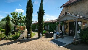 A stone building with a covered porch, a gravel driveway, and a garden with trees and shrubs. - Hôtel Bien-Etre Aux Cyprès de Marquay (Marquay)