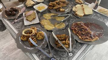 A buffet table with various food items including bread, pastries, and a pizza.