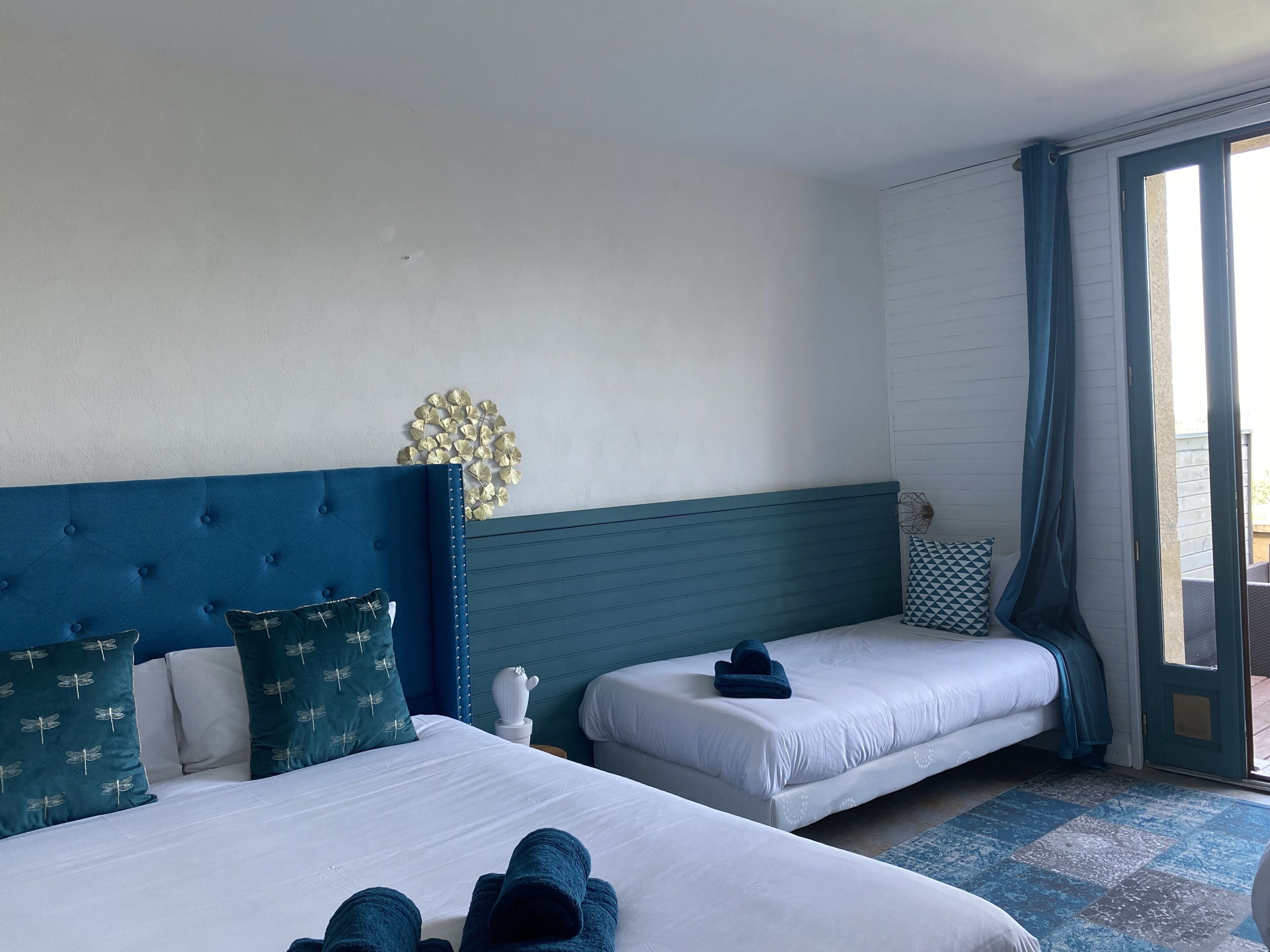 A hotel room with two beds, a decorative wall piece, and a view through a glass door.