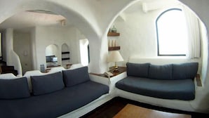 Un interior moderno con un sofá y una mesita, una ventana con cortinas, y una zona de cocina al fondo.