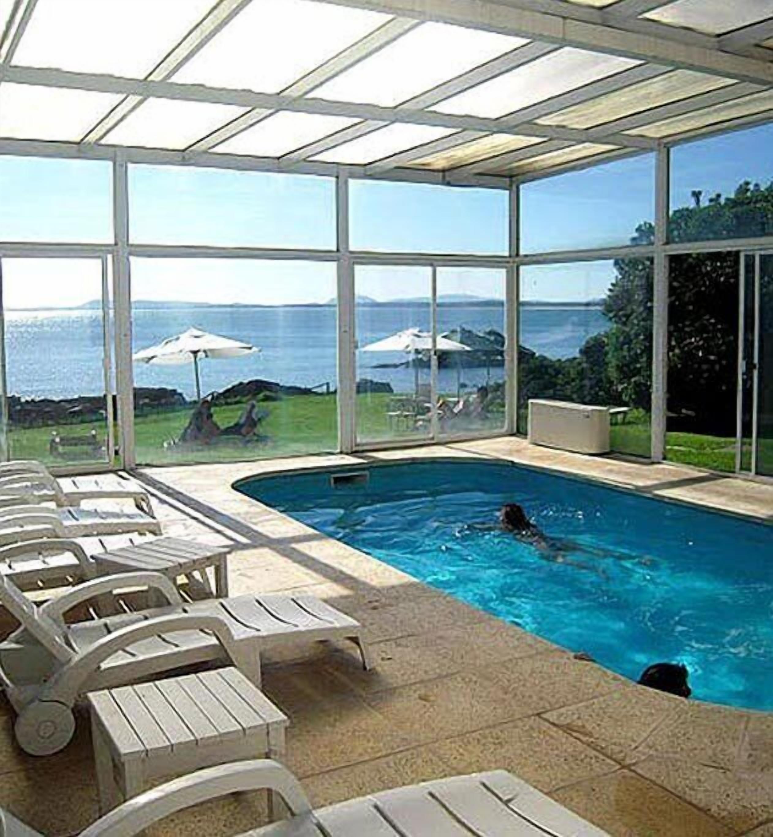 An indoor swimming pool with clear views of the sea and a grassy area with umbrellas.