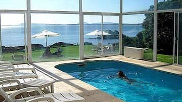 An indoor swimming pool with clear views of the sea and a grassy area with umbrellas.