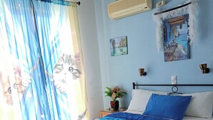 Un dormitorio con cama, cortinas, decoración en la pared, aire acondicionado y mesita de noche con un florero.