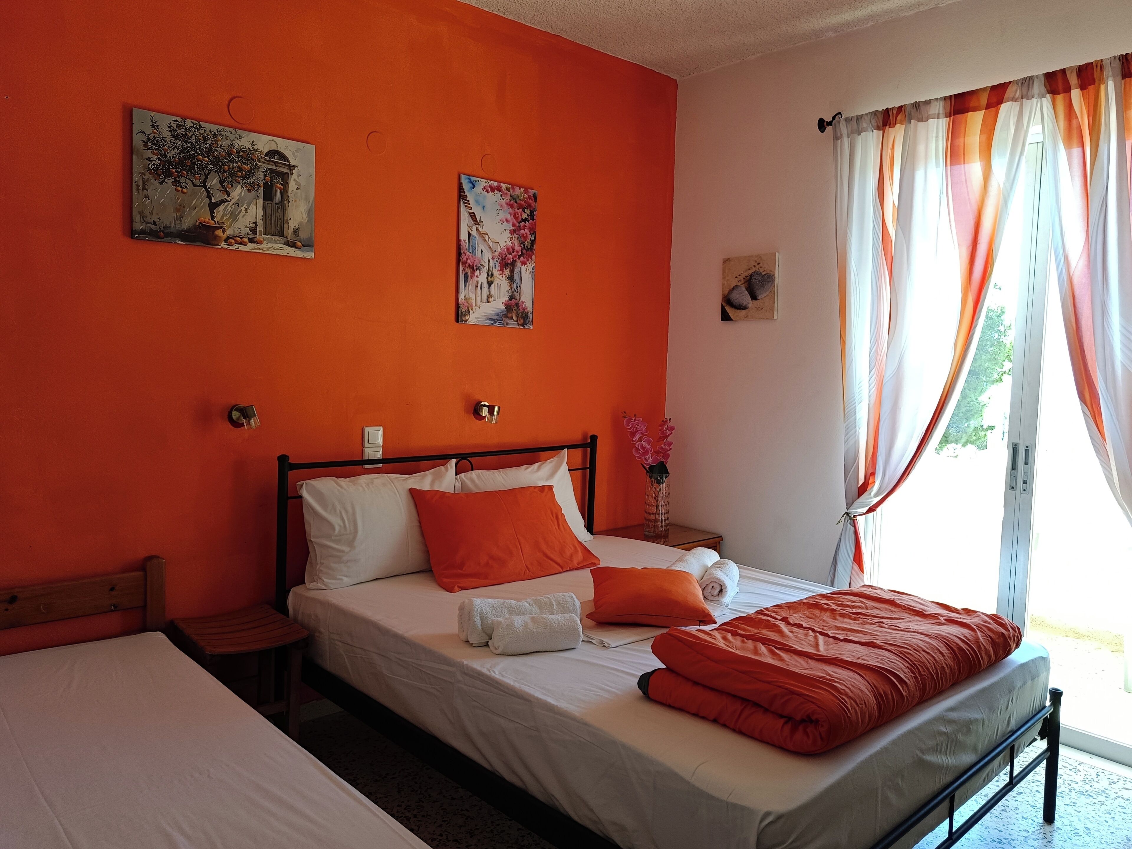 A room with a bed, a nightstand, a window with curtains, and two paintings on the wall.