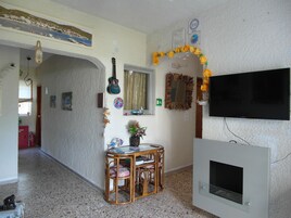 Una sala de estar con televisión, una guitarra, un espejo y una pequeña mesa con sillas.