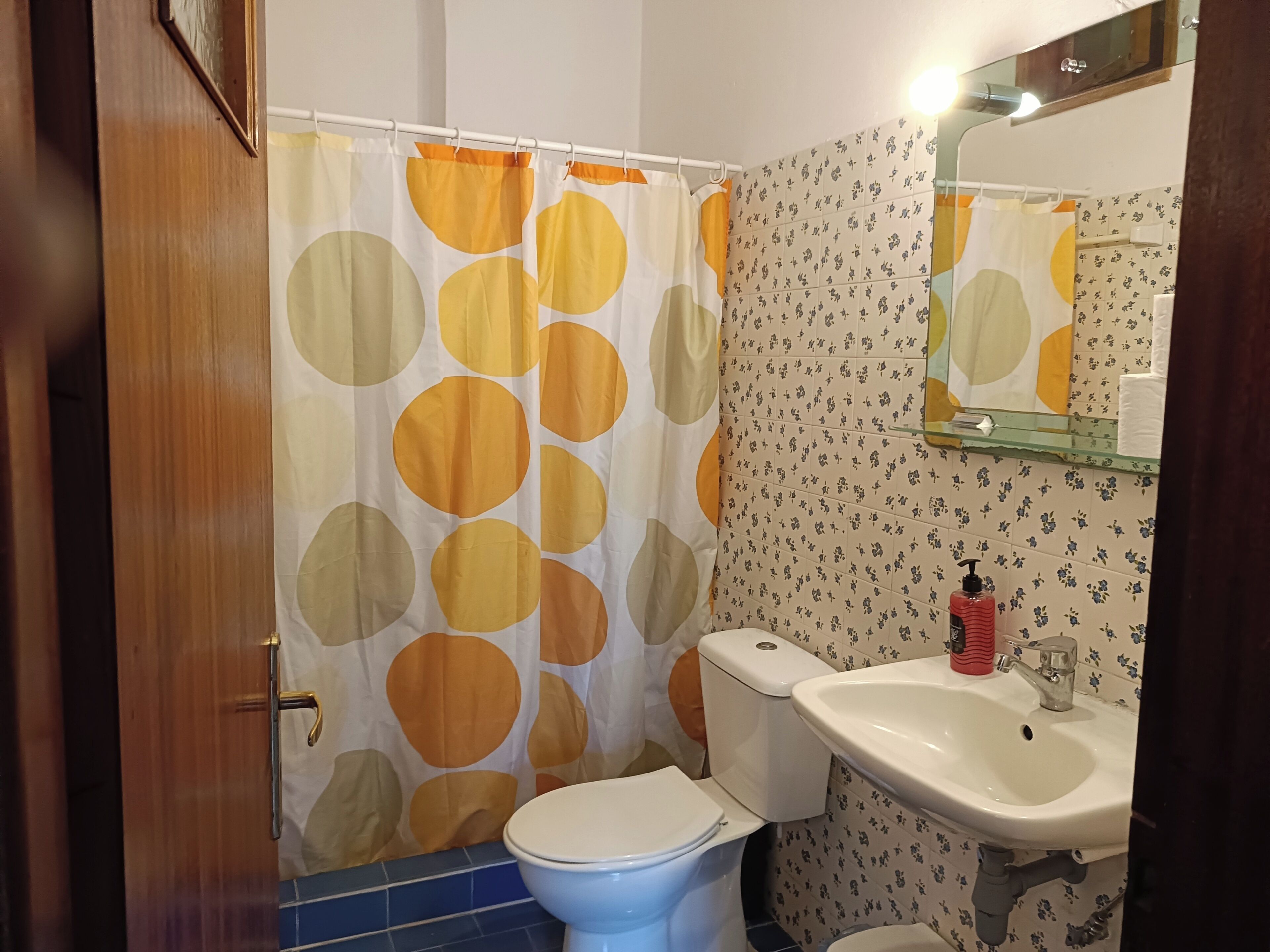 A bathroom with a toilet, sink, shower curtain with circular patterns, and a mirror above the sink.