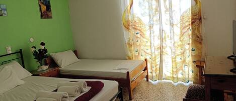 Une chambre avec deux lits, une petite table, une chaise, un climatiseur fixé au mur et une fenêtre agrémentée de rideaux décoratifs.
