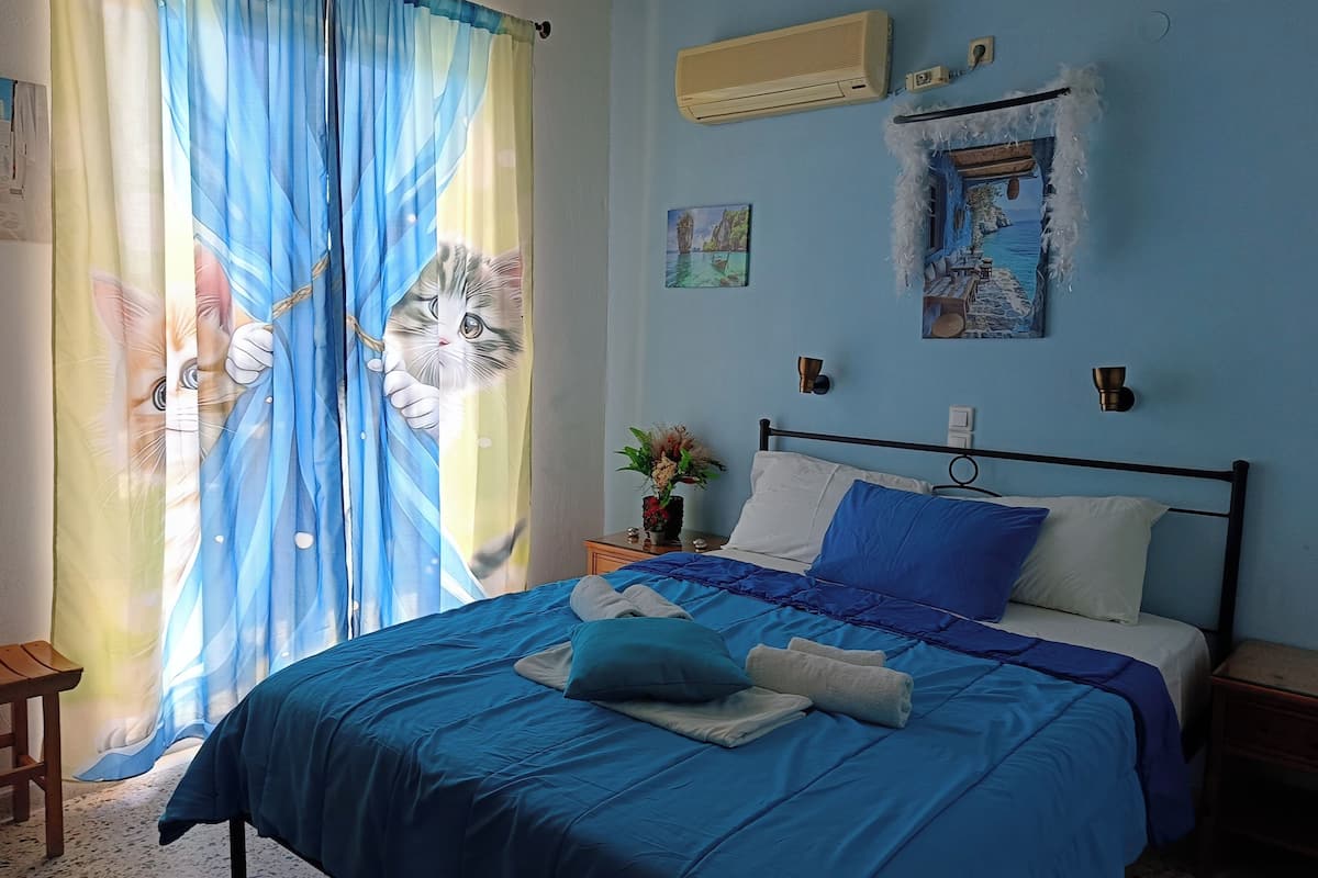 Un dormitorio con cama, cortinas, aire acondicionado, decoración en la pared y una mesita de noche.