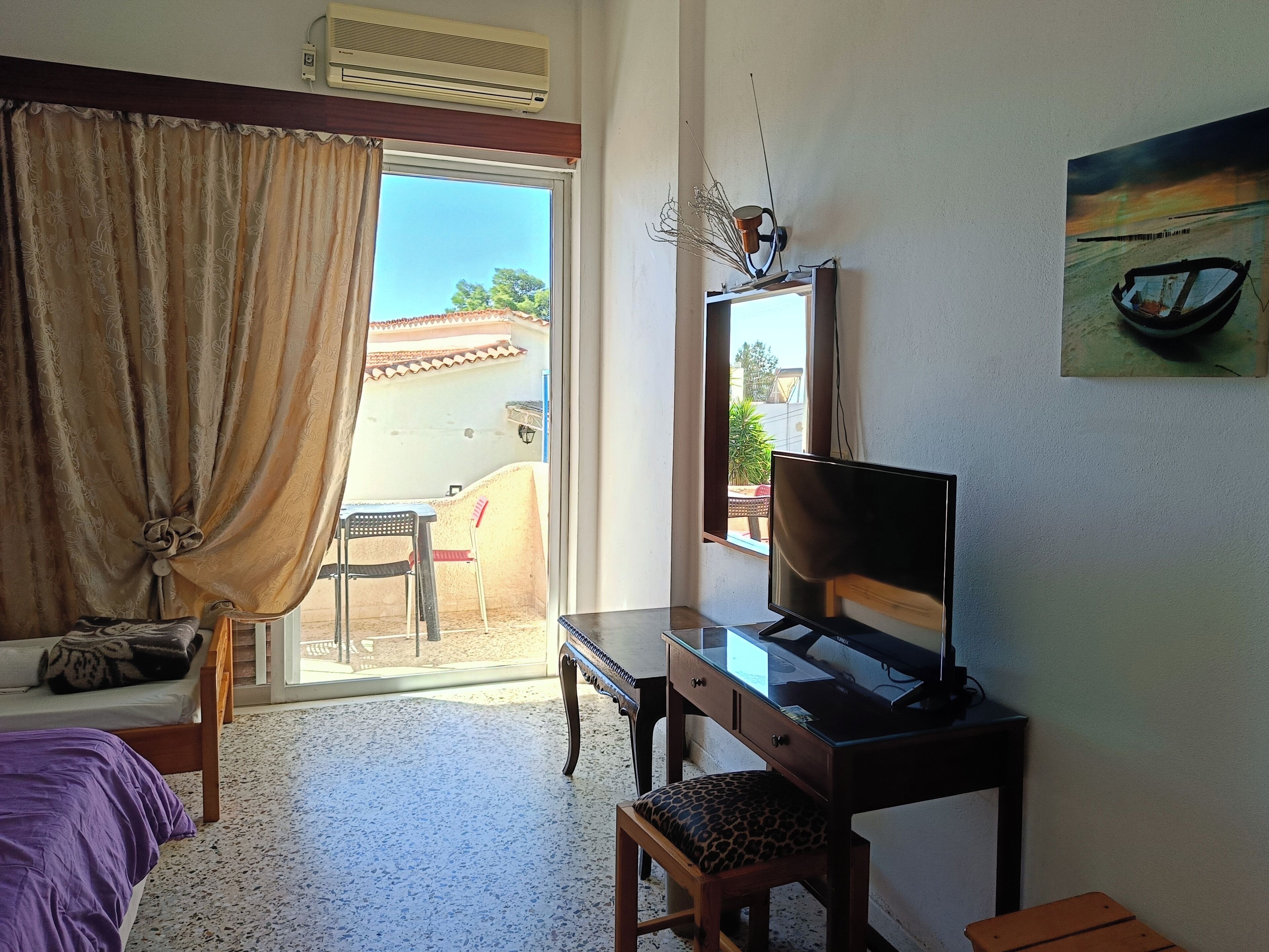 A hotel room with a bed, a desk with a television, a chair, a small table, and a view of the outside.
