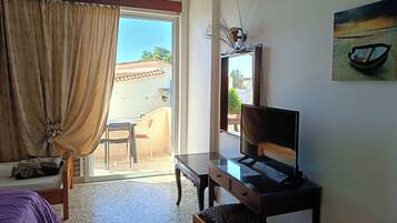 A hotel room with a bed, a desk with a television, a chair, a small table, and a view of the outside.