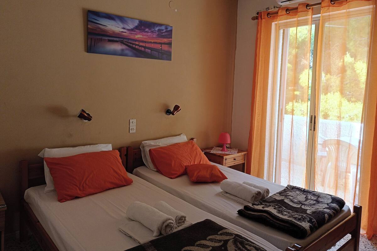Habitación de hotel con dos camas, un cuadro en la pared, una mesita de noche con lámpara y una ventana con cortinas.