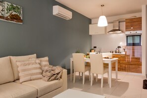 A modern living room with a sofa, dining table, and chairs. There is a kitchen area with cabinets and an oven.