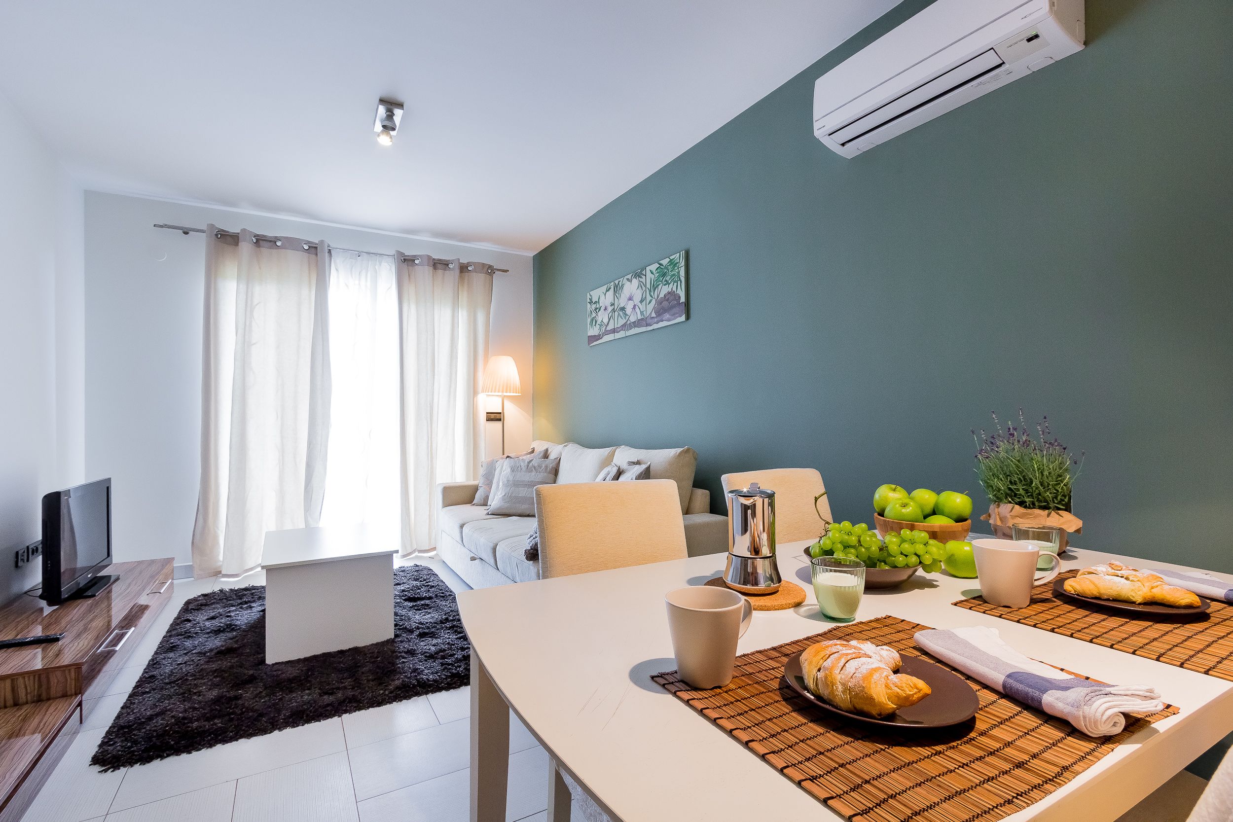 Een moderne woonkamer met een bank, een eettafel gedekt met eten en drinken, een televisie en een koffiezetapparaat.