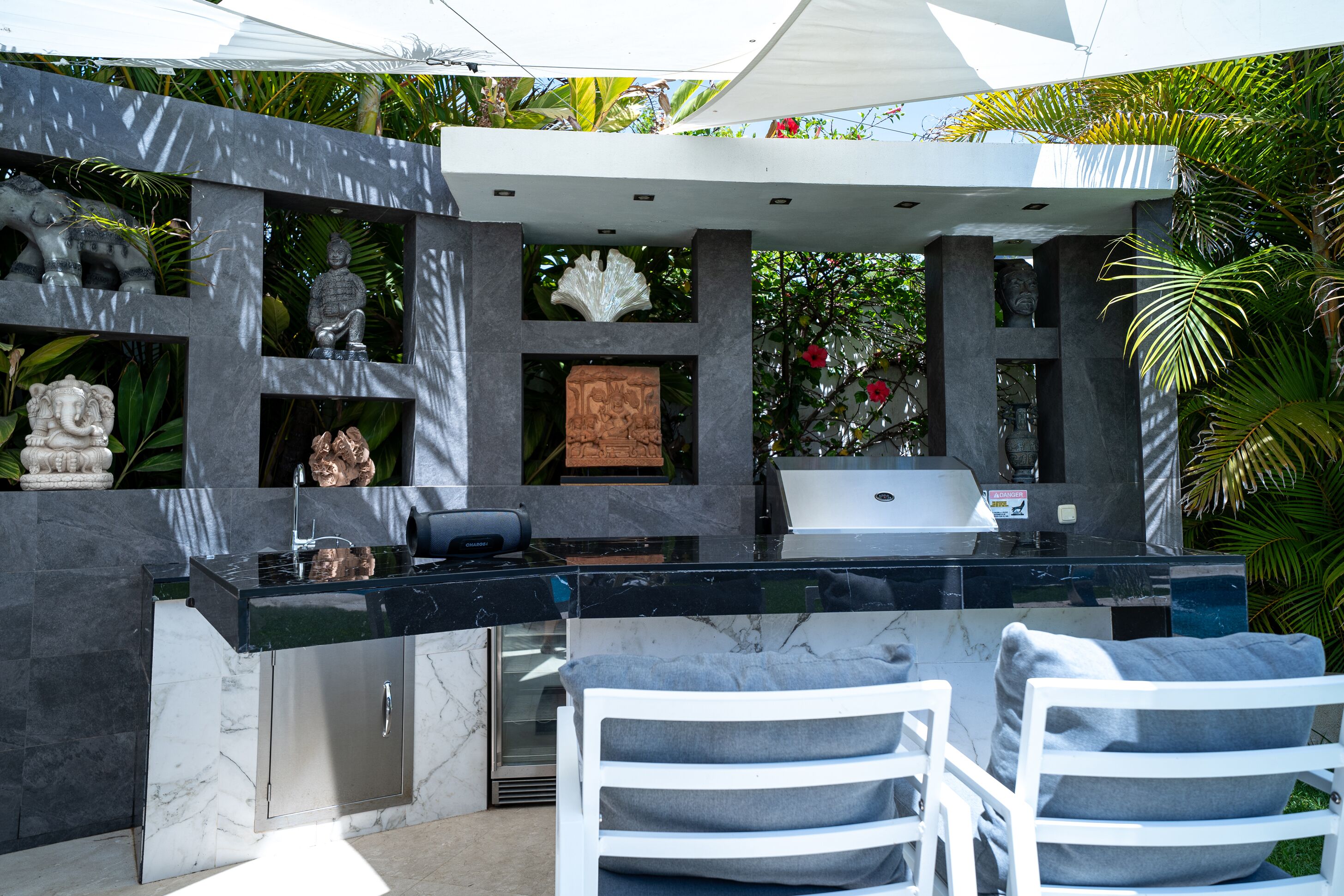 A modern outdoor kitchen with a black countertop, white chairs, and various decorative items.