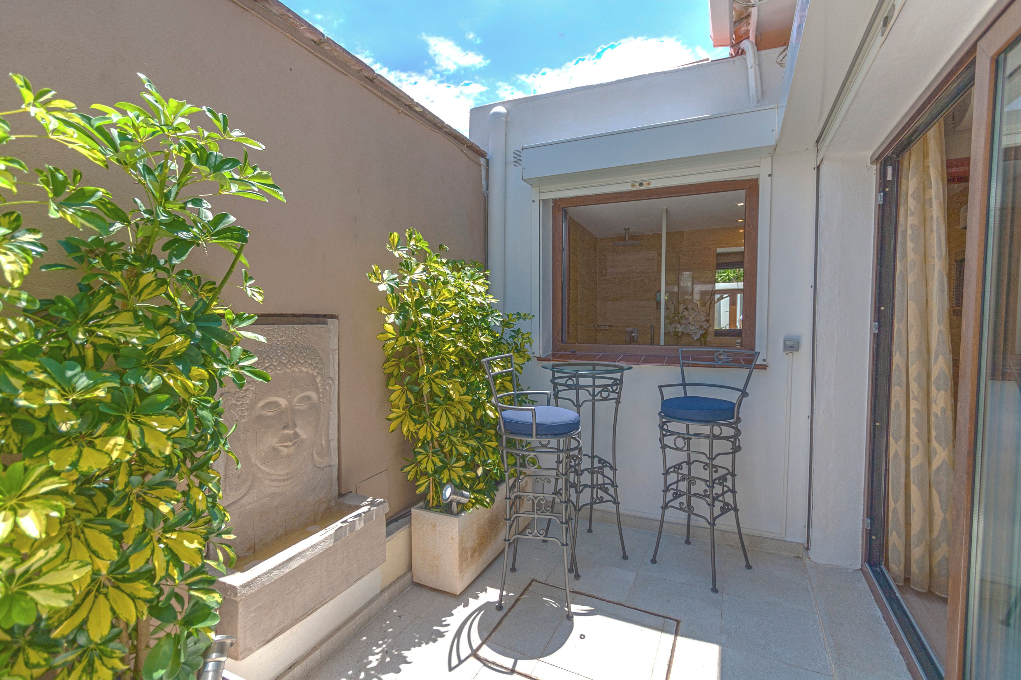 A small outdoor patio with a seating area, a window, and a Buddha statue.