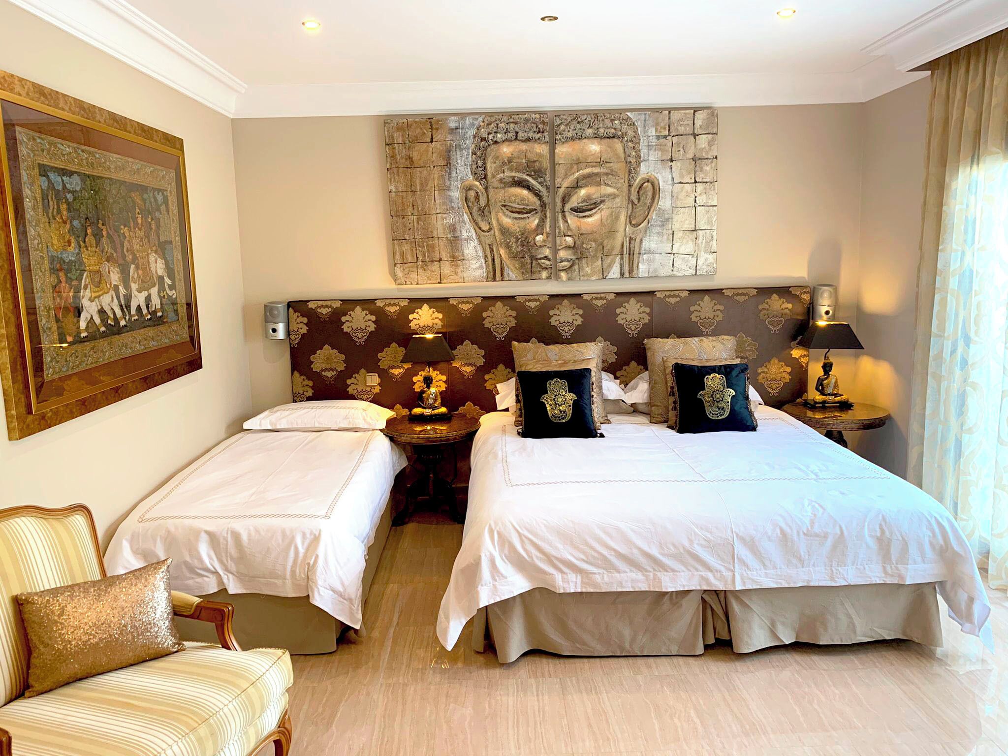 Une chambre d’hôtel avec deux lits, une grande statue de Bouddha accrochée au mur, un tableau encadré et une petite table avec une lampe.