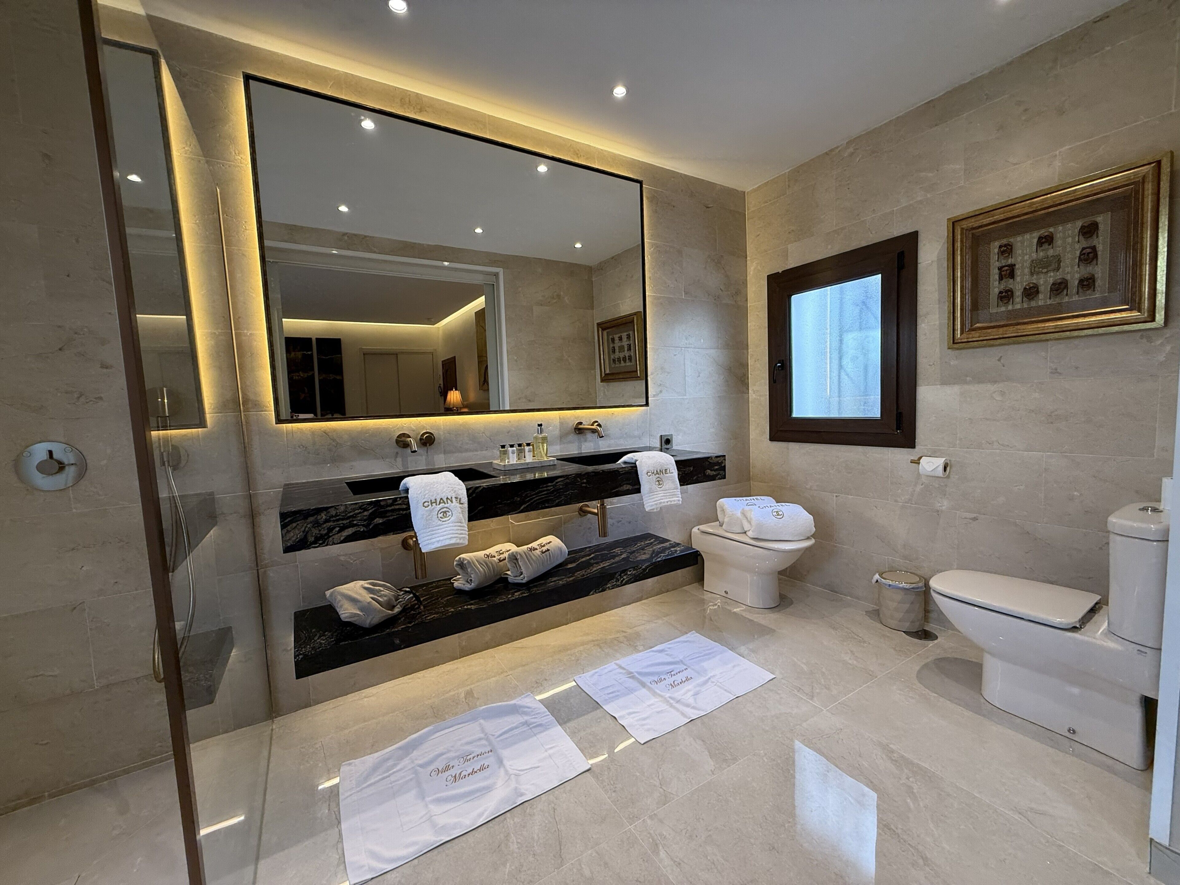 A modern bathroom with a large mirror, dual sinks, a toilet, and a shower area.